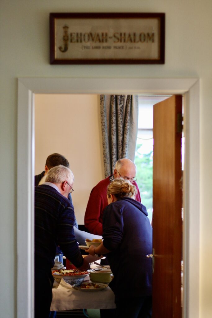 Members of the Harper family serving themselves food, viewed through a doorway with the words Jehovah Shalom written above it.