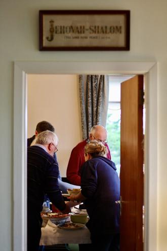 Members of the Harper family serving themselves food, viewed through a doorway with the words Jehovah Shalom written above it.