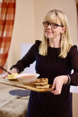 Patricia Harper holds a serving board with butter, soup and bread.